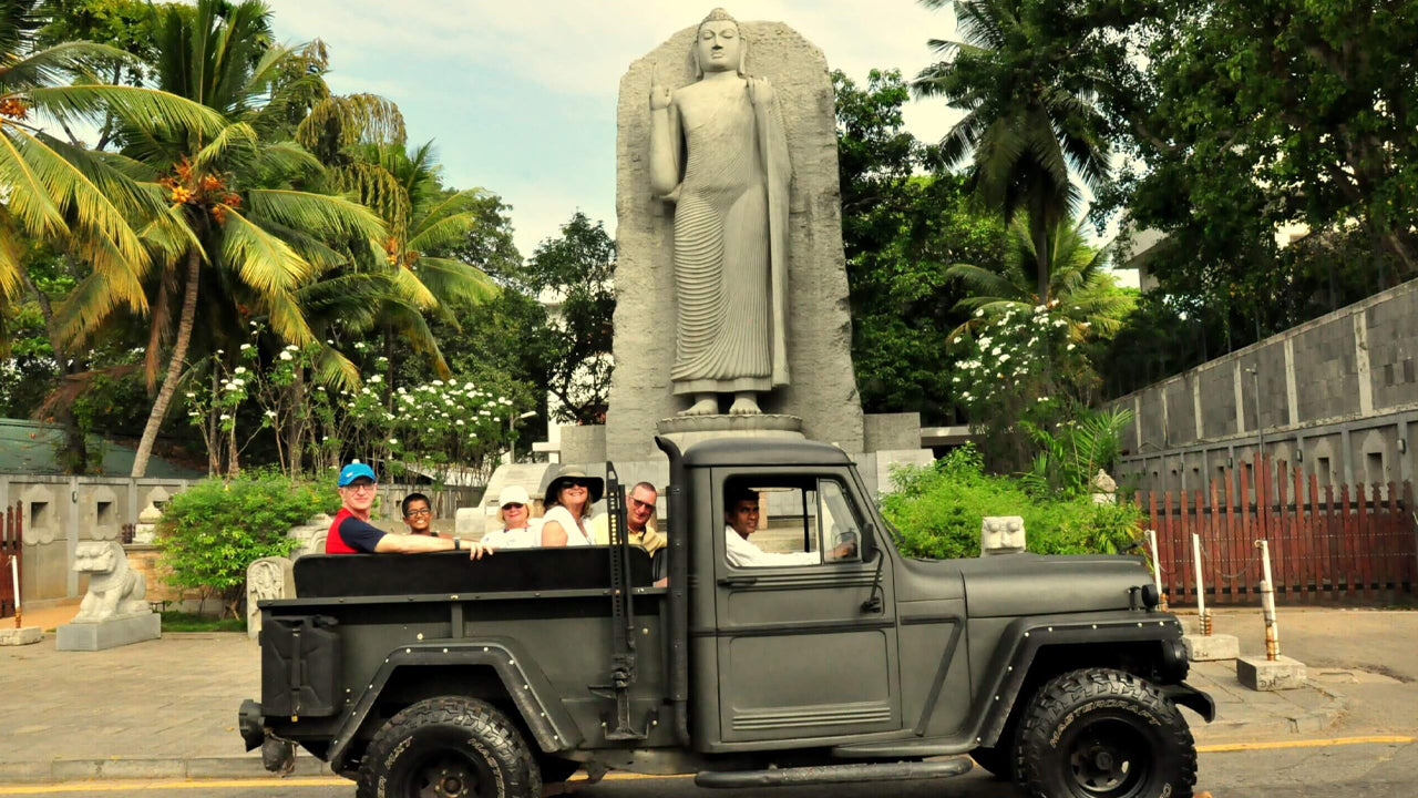 Vintage truck with passengers in front of a large statue in a park-like setting