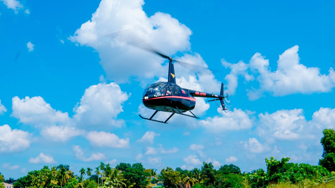 Helicopter flying in a clear blue sky with some clouds, surrounded by green trees.
